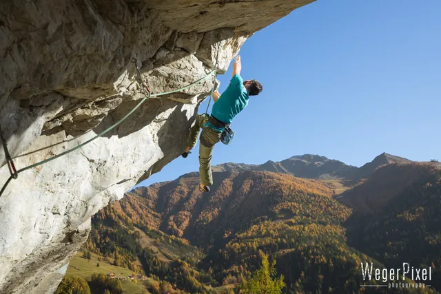 Kletterer im Überhang über einem herbstlichen Tal mit gelben Lärchen in Osttirol